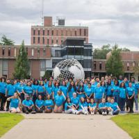A photo of the Urban Education Summer Bridge Program students wearing a turquoise-colored T-shirt and shorts. They pose in front of the campus globe, which features the brick Ely building in the background.